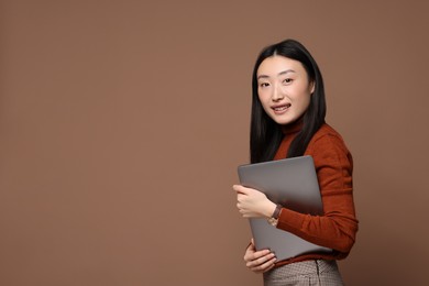 Portrait of smiling woman with laptop on brown background. Space for text