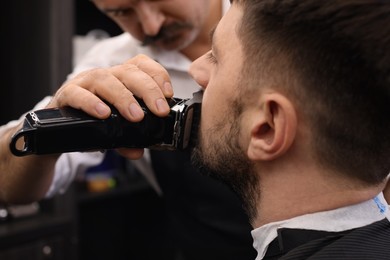 Photo of Professional hairdresser working with client in barbershop, closeup