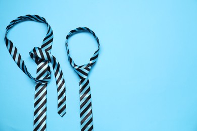 Striped neckties on light blue background, top view. Space for text