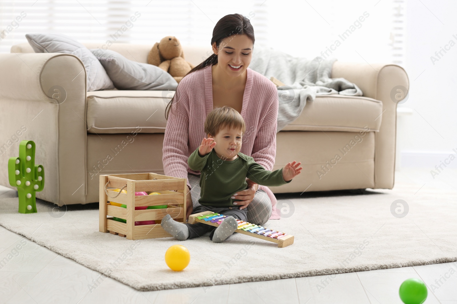 Photo of Young nanny and cute little baby playing with toys at home