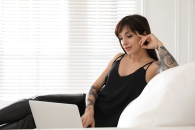 Photo of Beautiful woman with tattoos on arms using laptop in living room