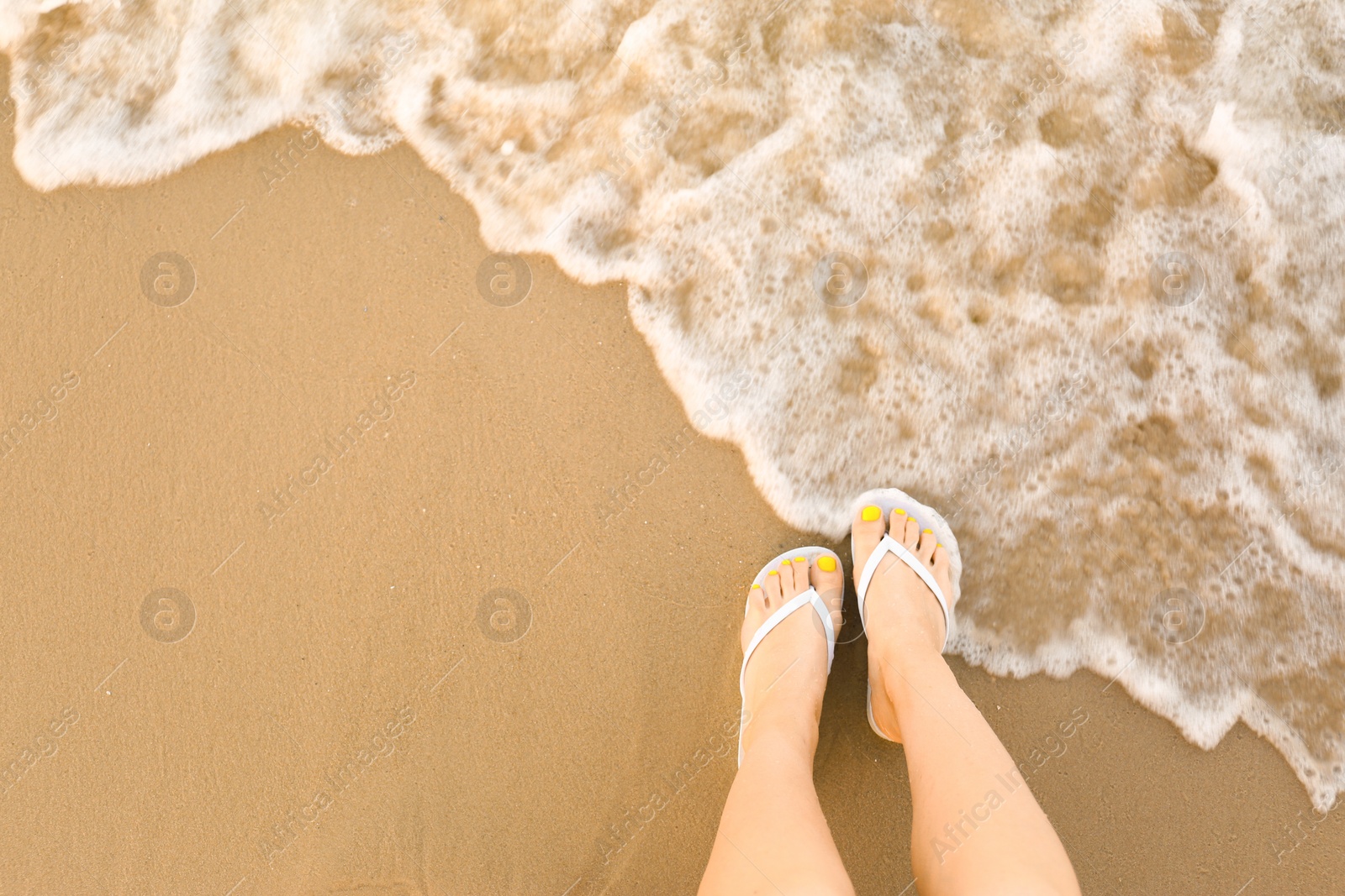 Photo of Top view of woman with white flip flops on sand near sea, space for text. Beach accessories