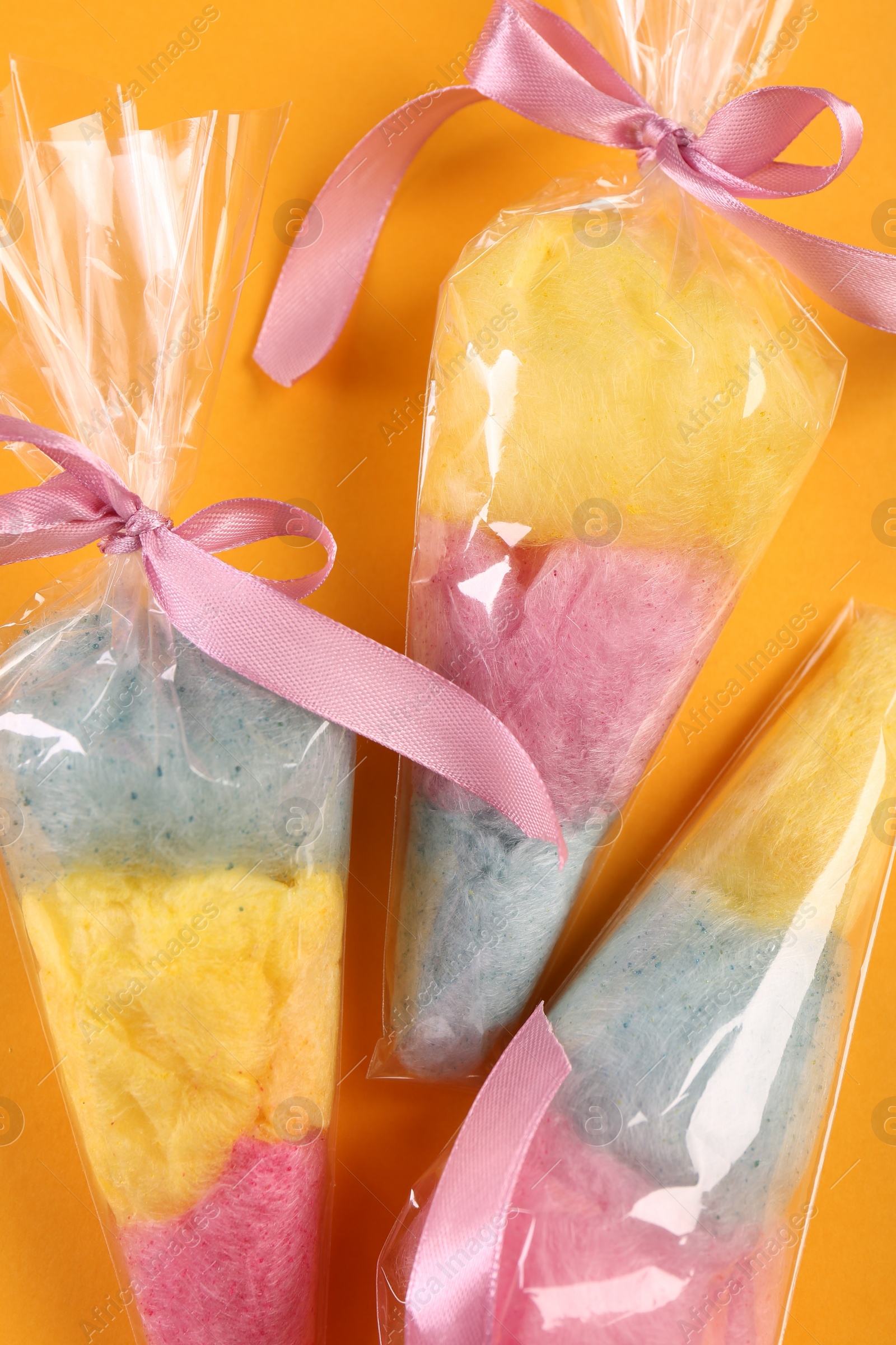 Photo of Packaged sweet cotton candies on orange background, flat lay
