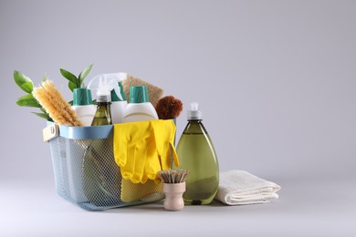 Set of different cleaning supplies in basket on light grey background