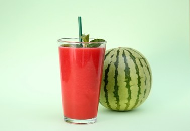 Glass of delicious drink with mint and fresh watermelon on light green background