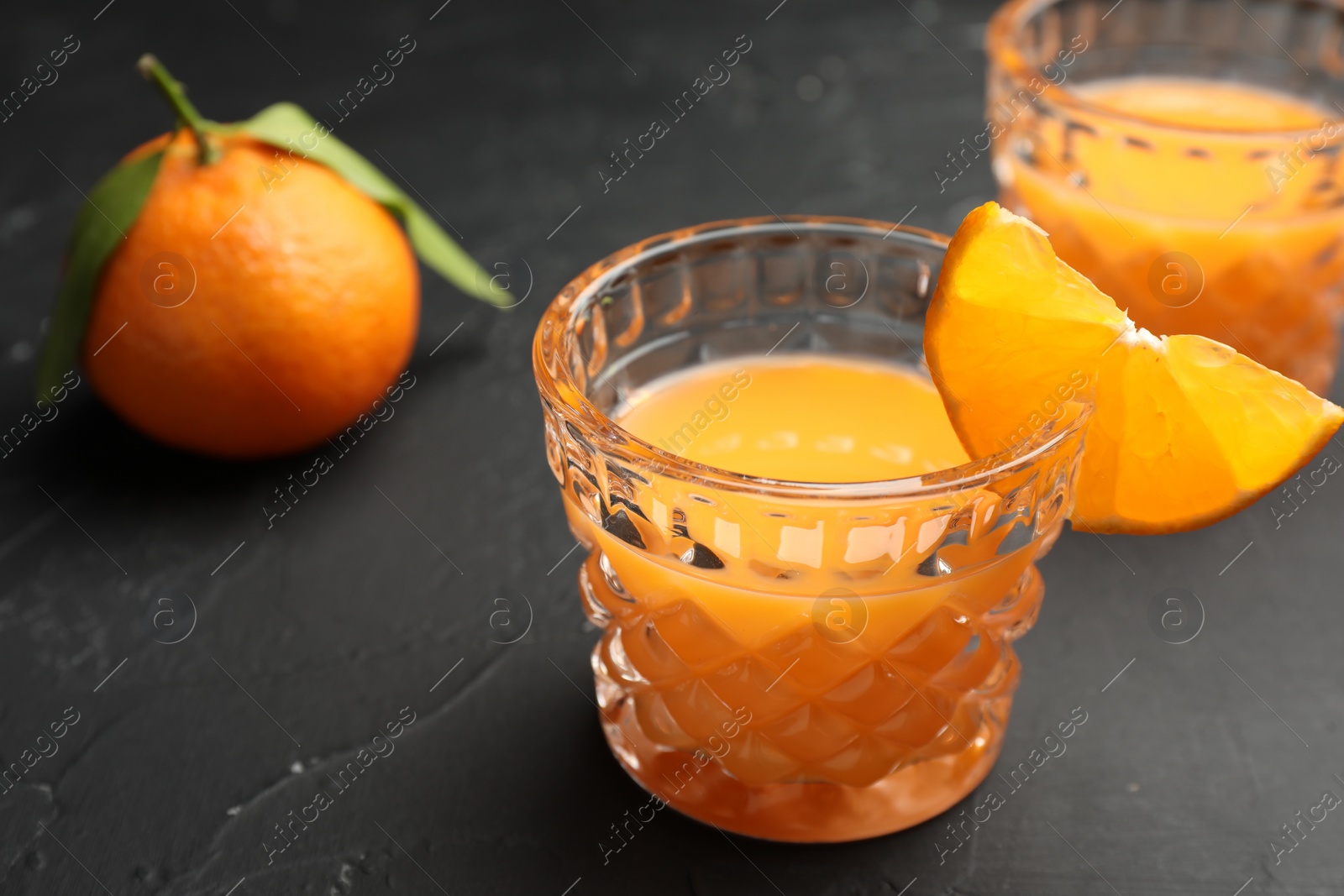 Photo of Tasty tangerine liqueur in glass and fresh citrus fruits on black textured table, closeup