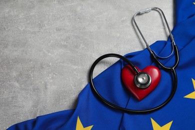 Photo of Stethoscope, red heart and flag of European Union on light grey table, flat lay. Space for text