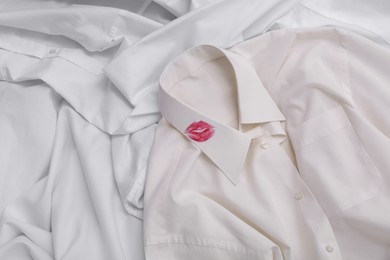 Photo of Men's shirt with lipstick kiss mark among other clothes as background