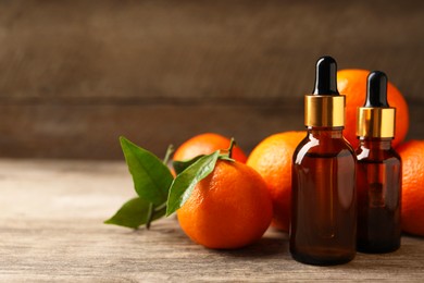 Bottles of tangerine essential oil and fresh fruits on wooden table, closeup. Space for text
