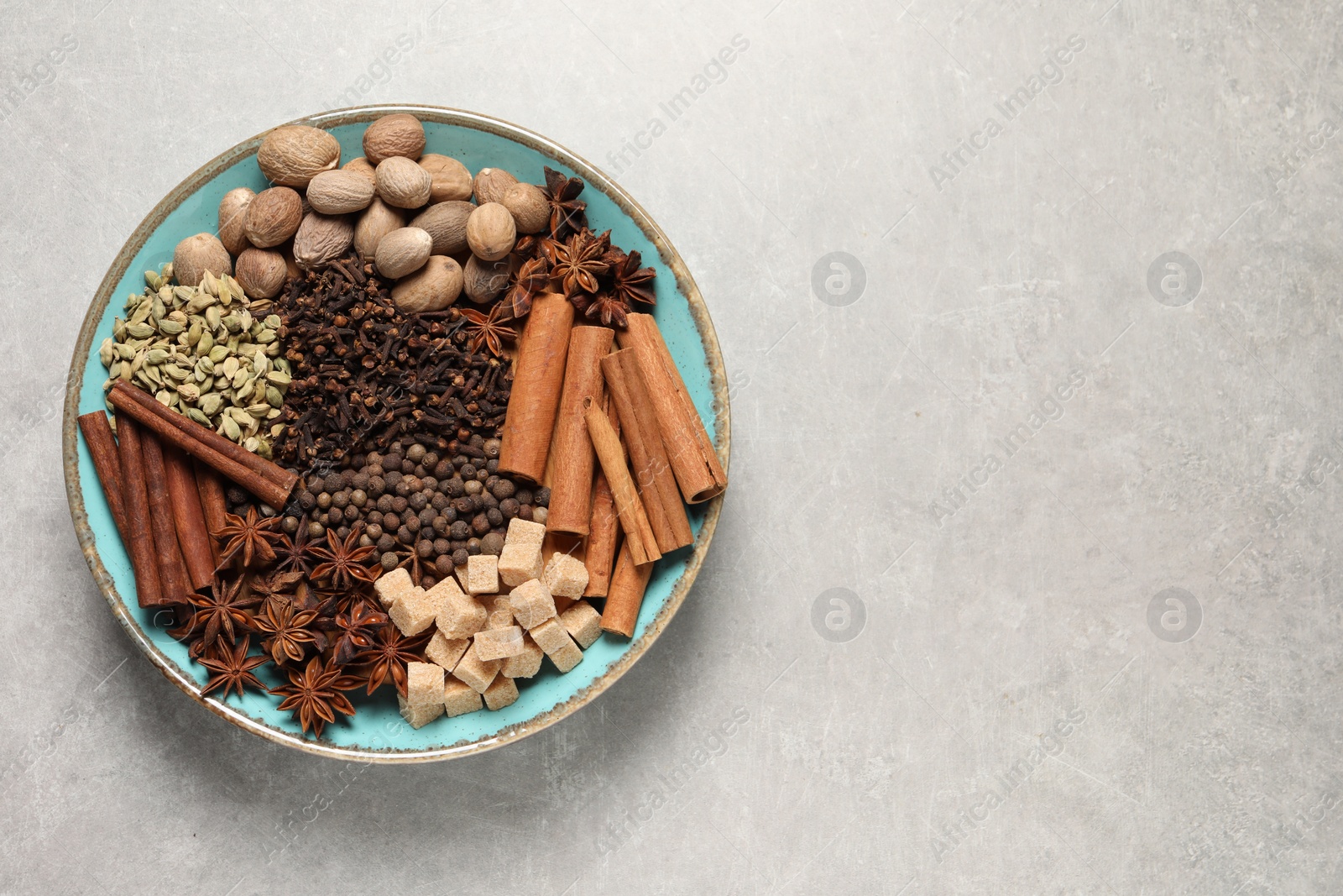 Photo of Different spices and nuts in bowl on light gray textured table, top view. Space for text