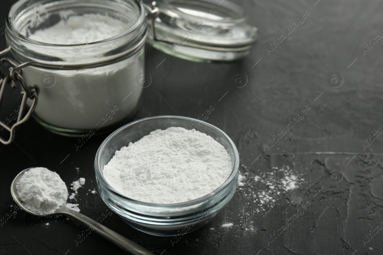 Photo of Baking powder in bowl, jar and spoon on black textured table, closeup. Space for text