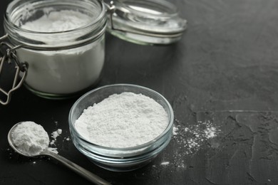 Baking powder in bowl, jar and spoon on black textured table, closeup. Space for text