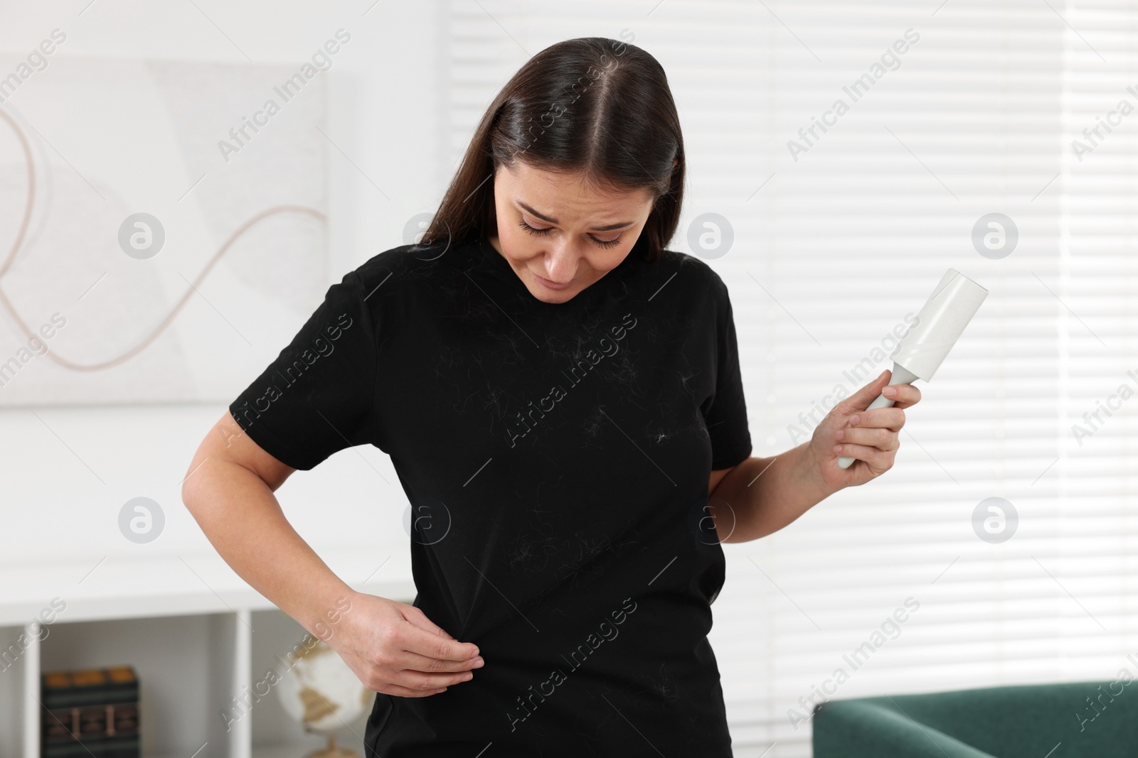 Photo of Woman with lint roller and pet hair on her black clothers at home