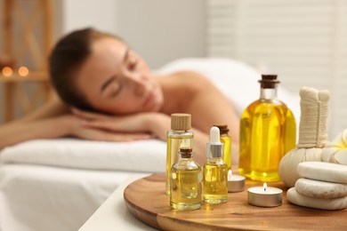 Photo of Aromatherapy. Woman relaxing on massage couch in spa salon, focus on bottles of essential oils, herbal bag, burning candle and stones