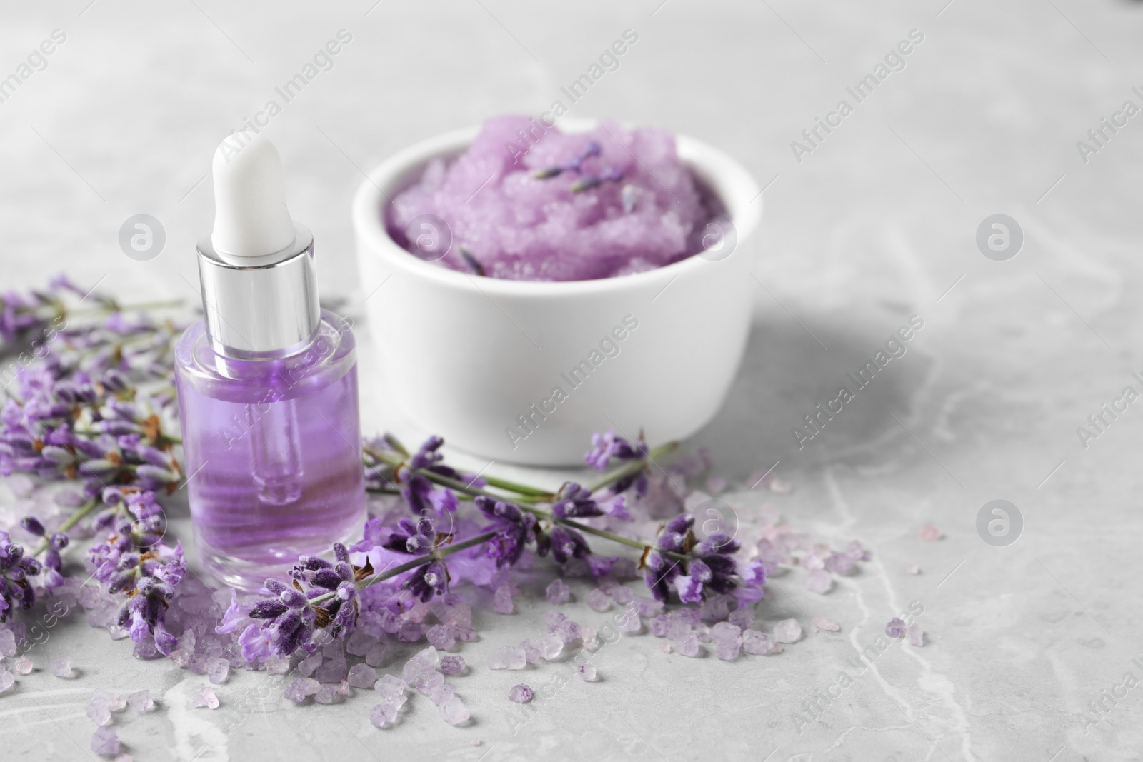 Photo of Natural cosmetic oil, bath salt, scrub and lavender flowers on grey marble table, space for text