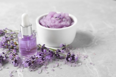 Photo of Natural cosmetic oil, bath salt, scrub and lavender flowers on grey marble table, space for text