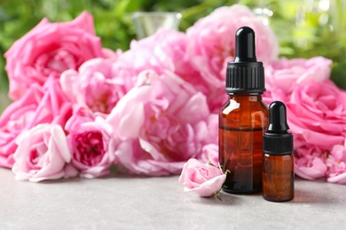 Photo of Bottles of rose essential oil and fresh flowers on grey table, space for text