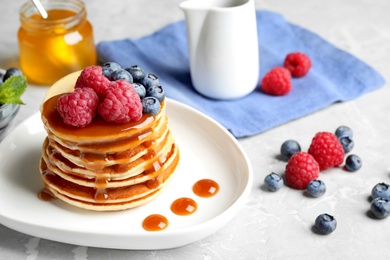 Delicious pancakes with fresh berries and syrup on grey table