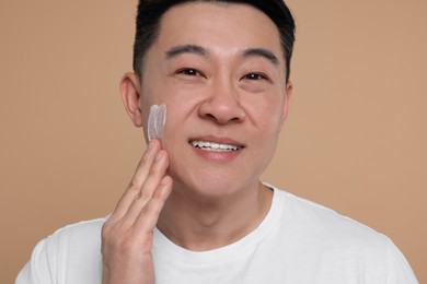 Photo of Handsome man applying cream onto his face on light brown background