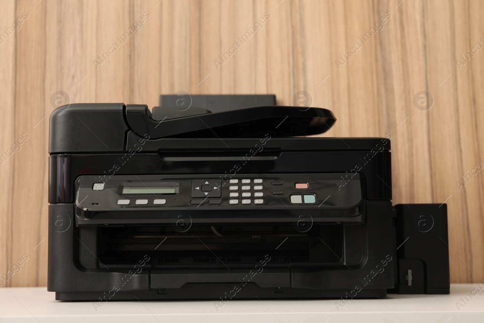 Photo of New modern printer on white table against wooden background