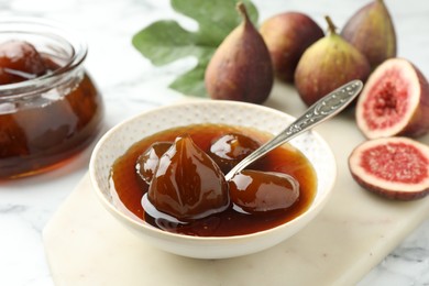 Bowl of tasty sweet jam and fresh figs on white marble table