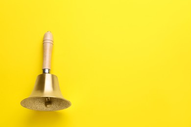 Photo of Golden school bell with wooden handle on yellow background, top view. Space for text
