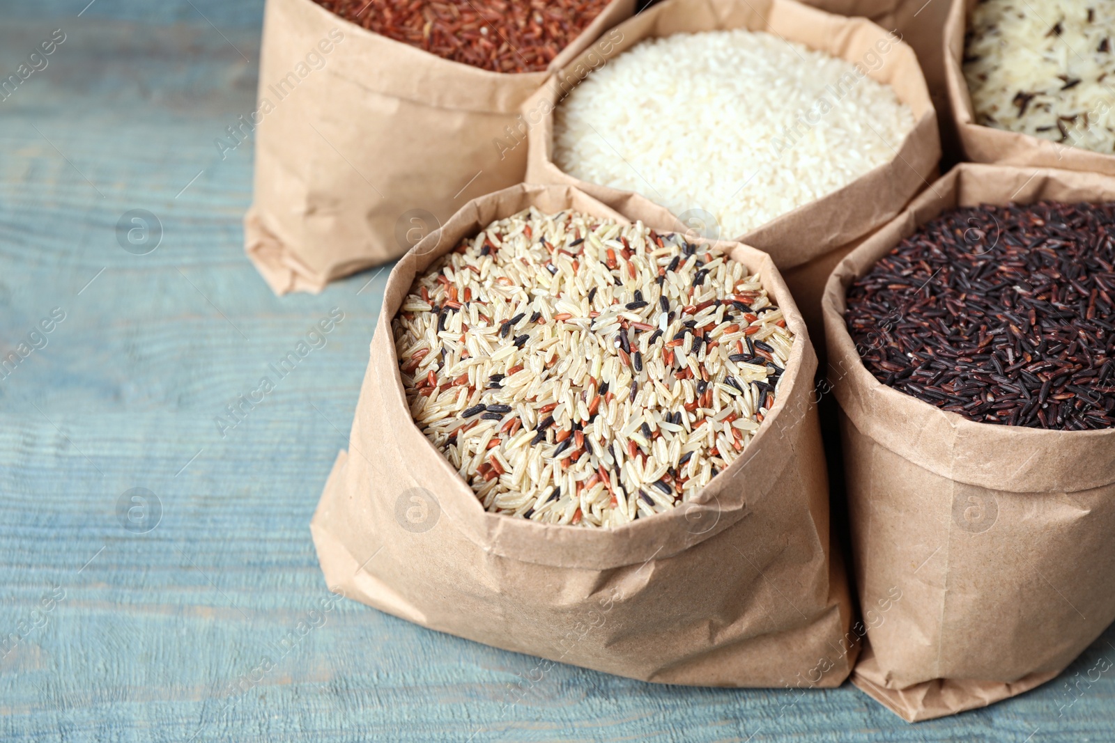 Photo of Brown and polished rice in paper bags on blue wooden table