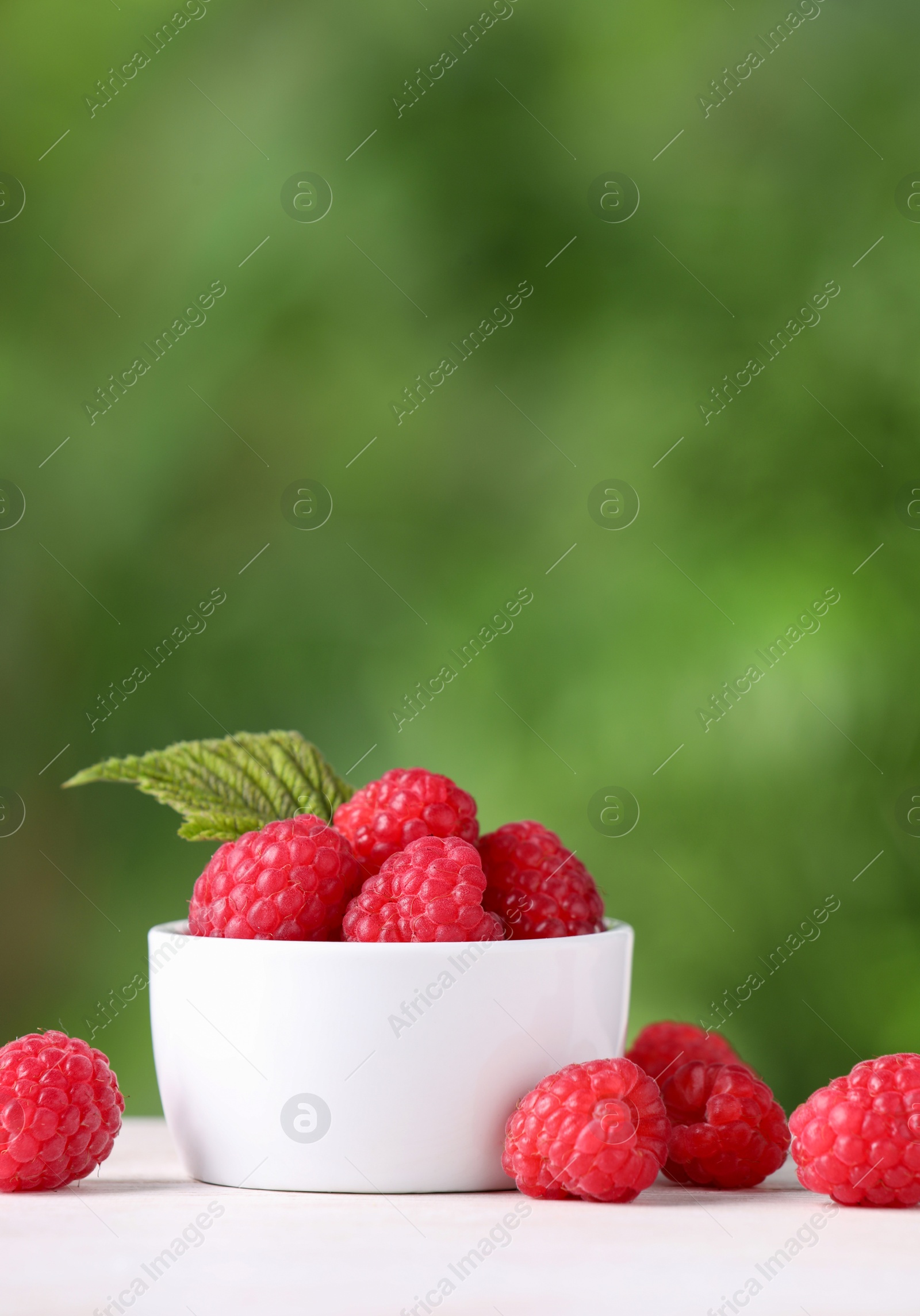 Photo of Tasty ripe raspberries and green leaf on white table outdoors. Space for text