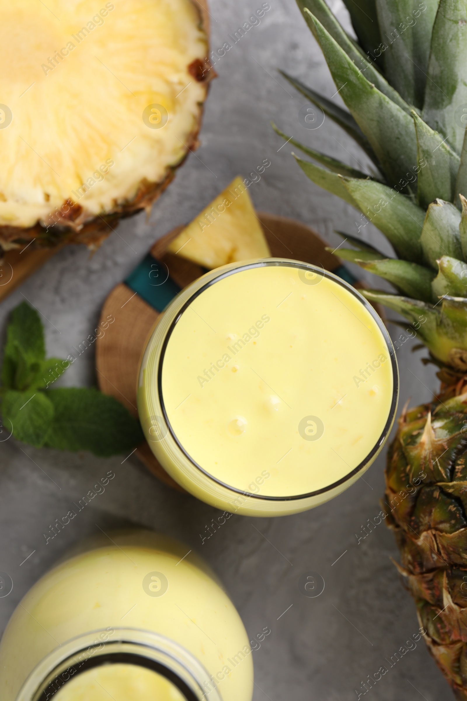 Photo of Tasty pineapple smoothie, mint and fruit on grey textured table, flat lay