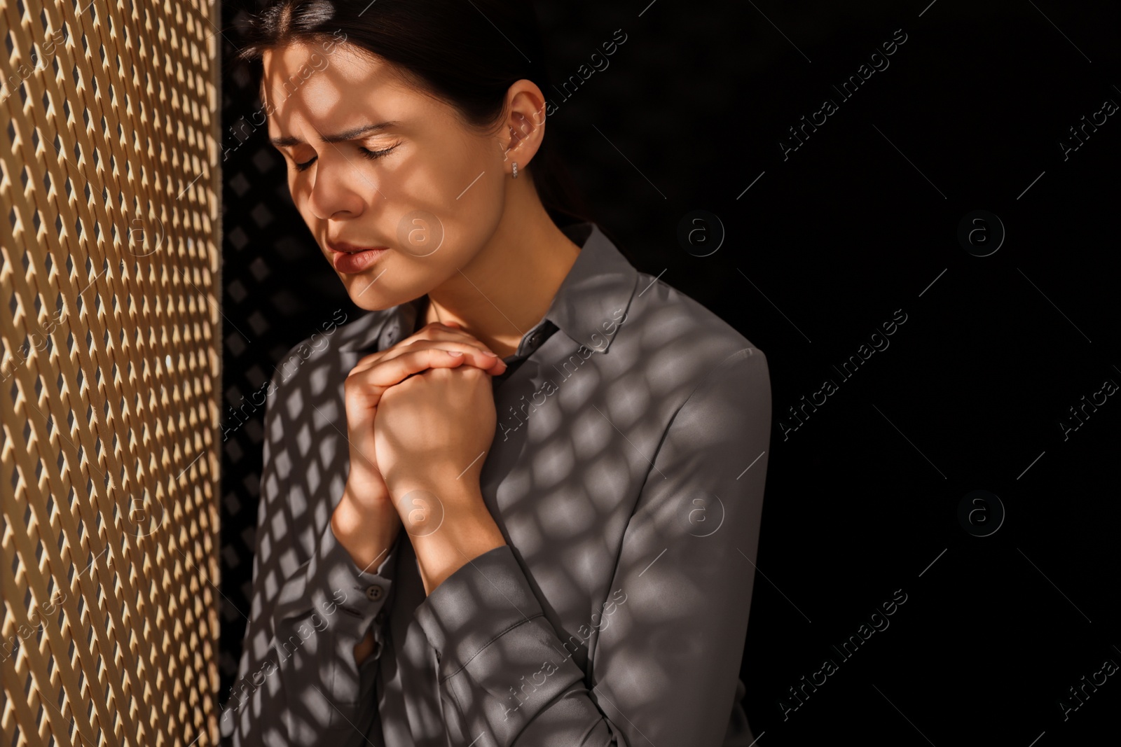 Photo of Upset woman listening to priest during confession near wooden partition in booth, space for text