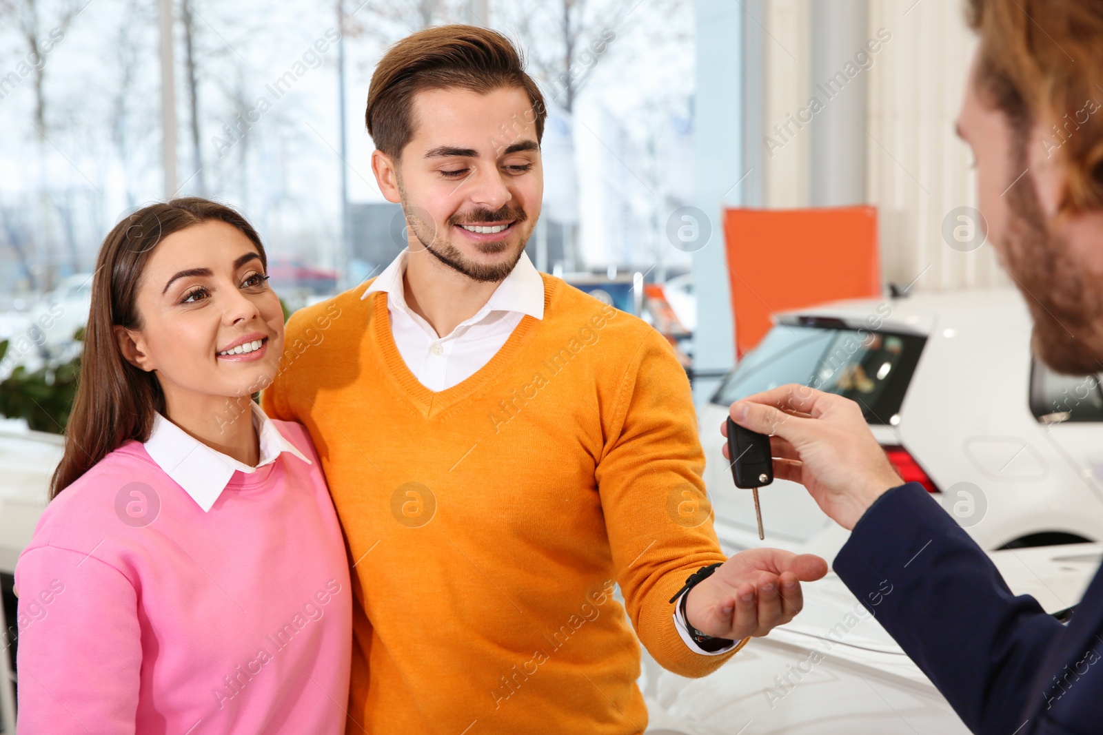 Photo of Car salesman giving key to couple in dealership