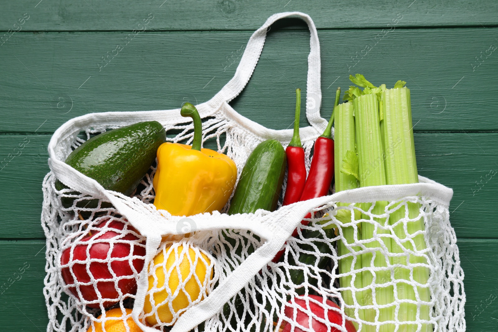 Photo of String bag with different vegetables on green wooden table, top view