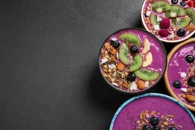 Photo of Acai smoothie bowls with granola and fruits on black table, flat lay. Space for text