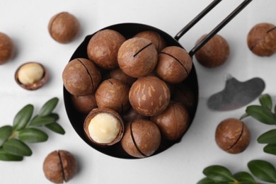 Photo of Tasty Macadamia nuts and green twigs on white table, flat lay