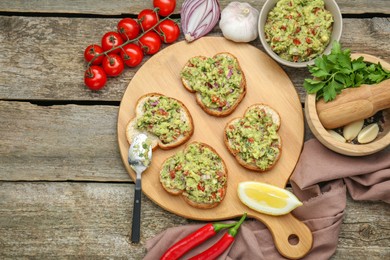 Photo of Slices of bread with tasty guacamole and ingredients on wooden table, flat lay. Space for text