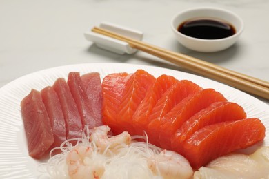 Photo of Tasty salmon slices, shrimp, funchosa and tuna on table, closeup. Delicious sashimi dish