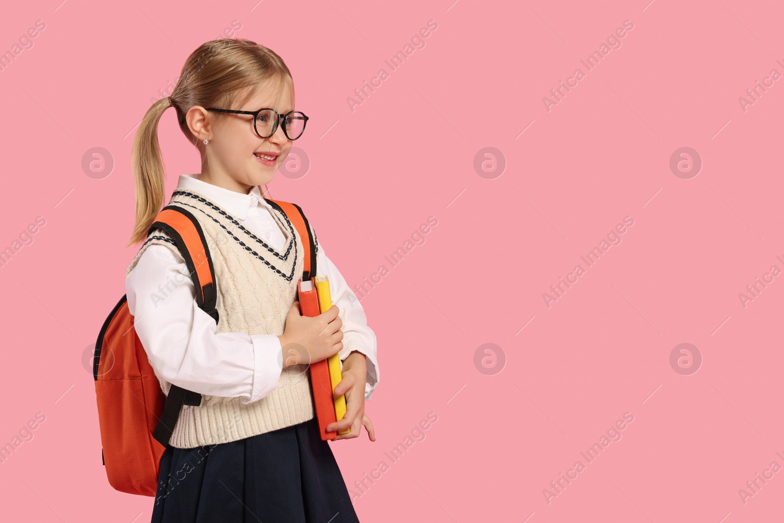 Photo of Happy schoolgirl in glasses with backpack and books on pink background, space for text