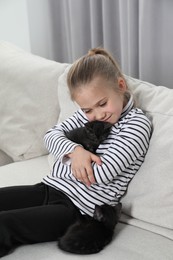 Photo of Little girl with cute fluffy kittens on sofa indoors