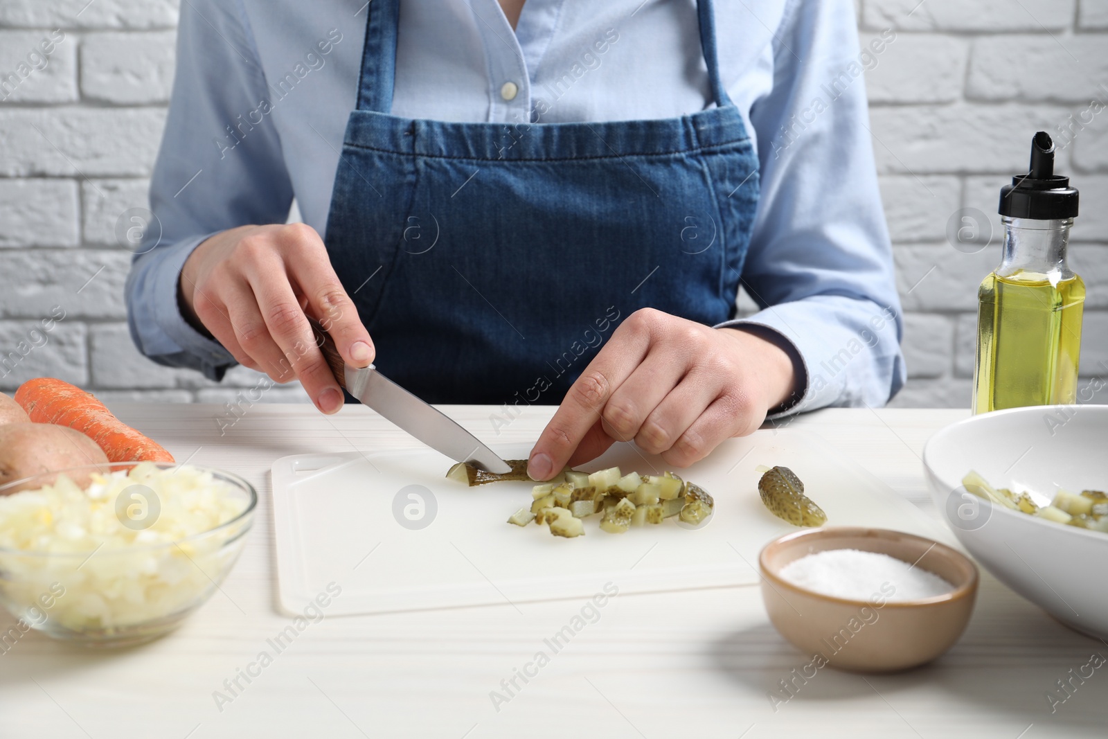 Photo of Woman cutting pickled cucumbers at white wooden table, closeup. Cooking vinaigrette salad