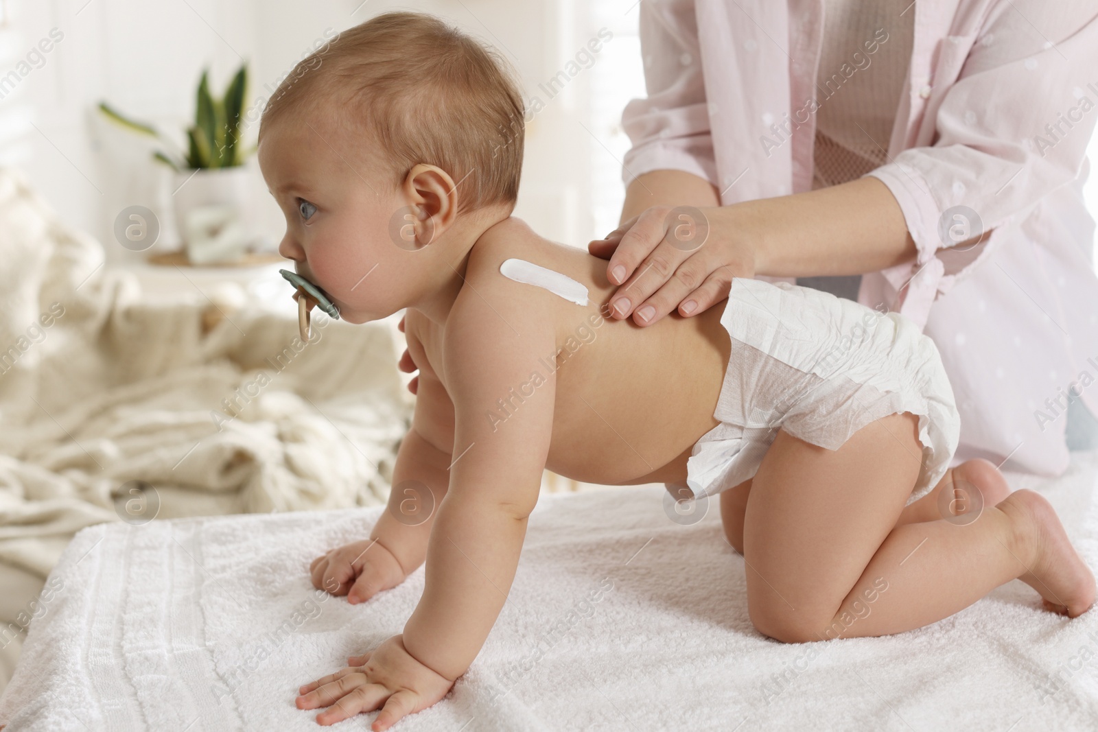 Photo of Mother applying body cream on her little baby at home, closeup