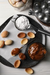 Delicious walnut shaped cookies with condensed milk on white wooden table, flat lay