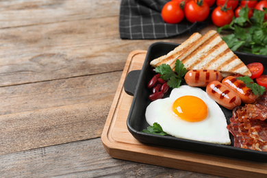 Photo of Tasty breakfast with heart shaped fried egg and  sausages on wooden table, closeup