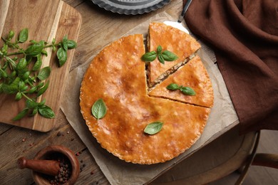 Delicious pie with meat and basil on wooden table, flat lay