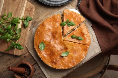 Photo of Delicious pie with meat and basil on wooden table, flat lay