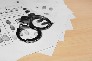 Photo of Police handcuffs and criminal fingerprints card on wooden background, space for text