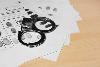 Police handcuffs and criminal fingerprints card on wooden background, space for text