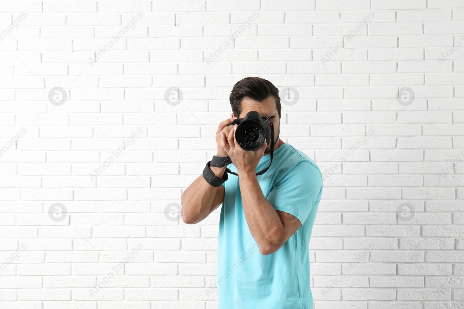 Photo of Young professional photographer taking picture near brick wall. Space for text