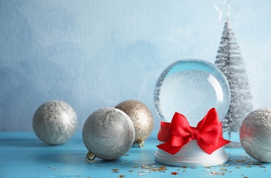 Photo of Empty snow globe with red bow and Christmas decorations on table. Space for text