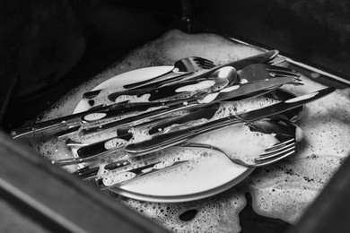 Photo of Washing silver spoons, forks and knives in kitchen sink with foam