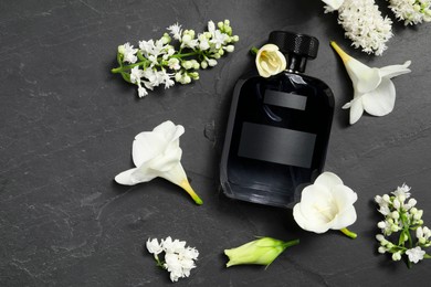 Bottle of luxury perfume and floral decor on black table, flat lay. Space for text